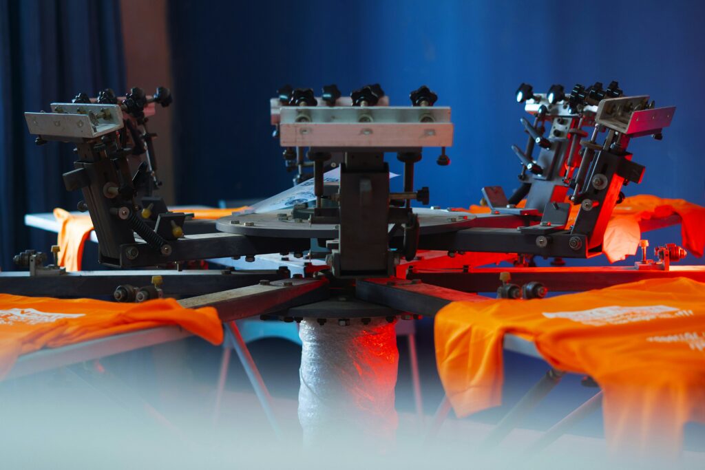 A machine printing on orange t-shirts showing DTG vs DTF printing.